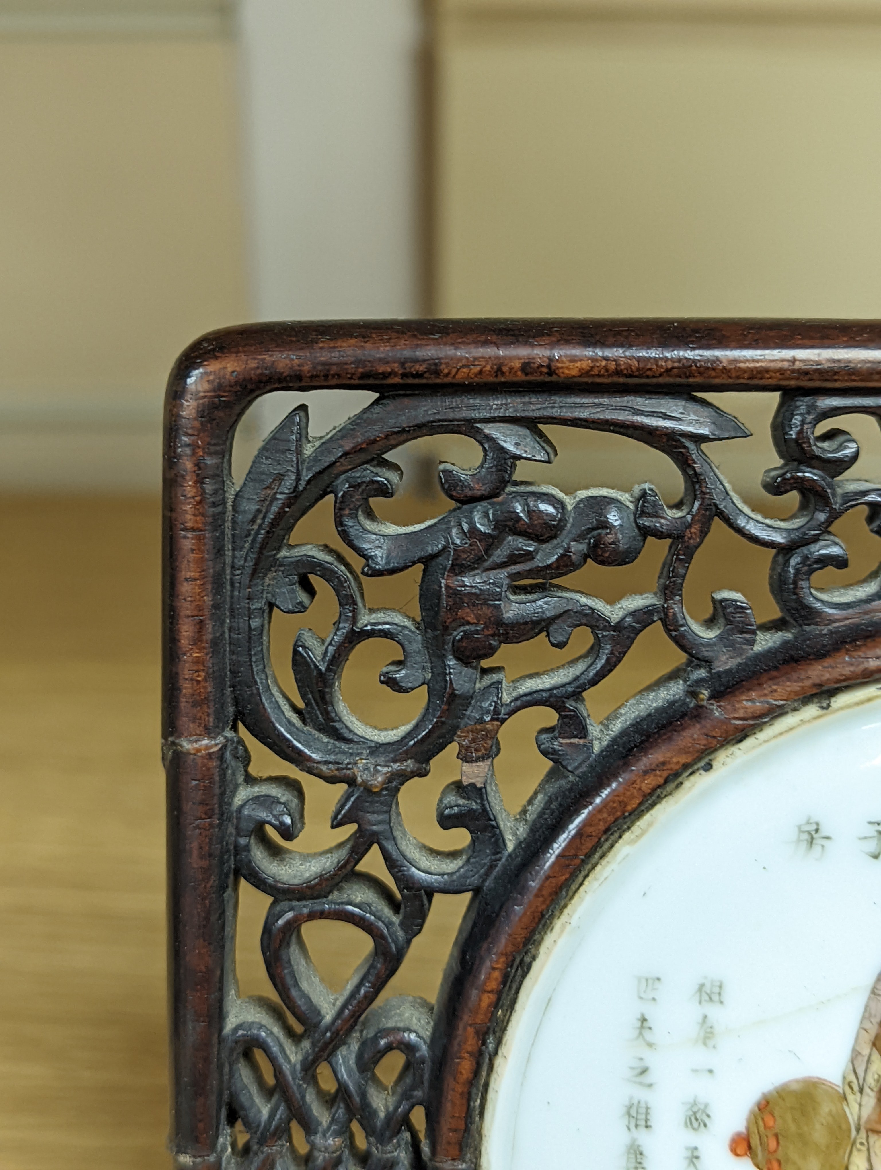 A 19th century Chinese famille rose circular plaque or cover, inset into a wood surround, cracks 15cm sq